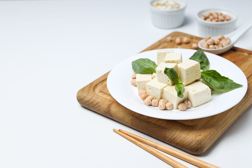 Zdjęcie tofu w kostkach na drewnianej desce. Tofu stanowi bogate źródło białka w diecie wegańskiej. Doskonale sprawdza się także w cateringu dietetycznym, zapewniając różnorodność potraw.